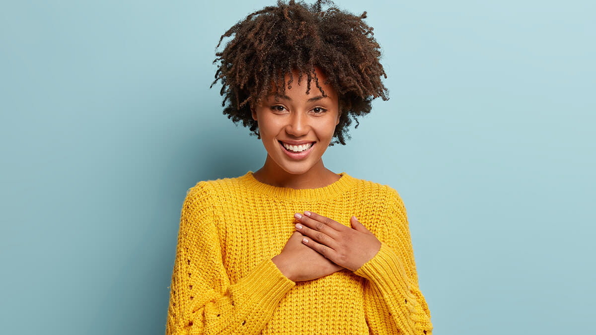 Portrait of a smiling Black woman in a yellow sweater, warm and grateful mood.