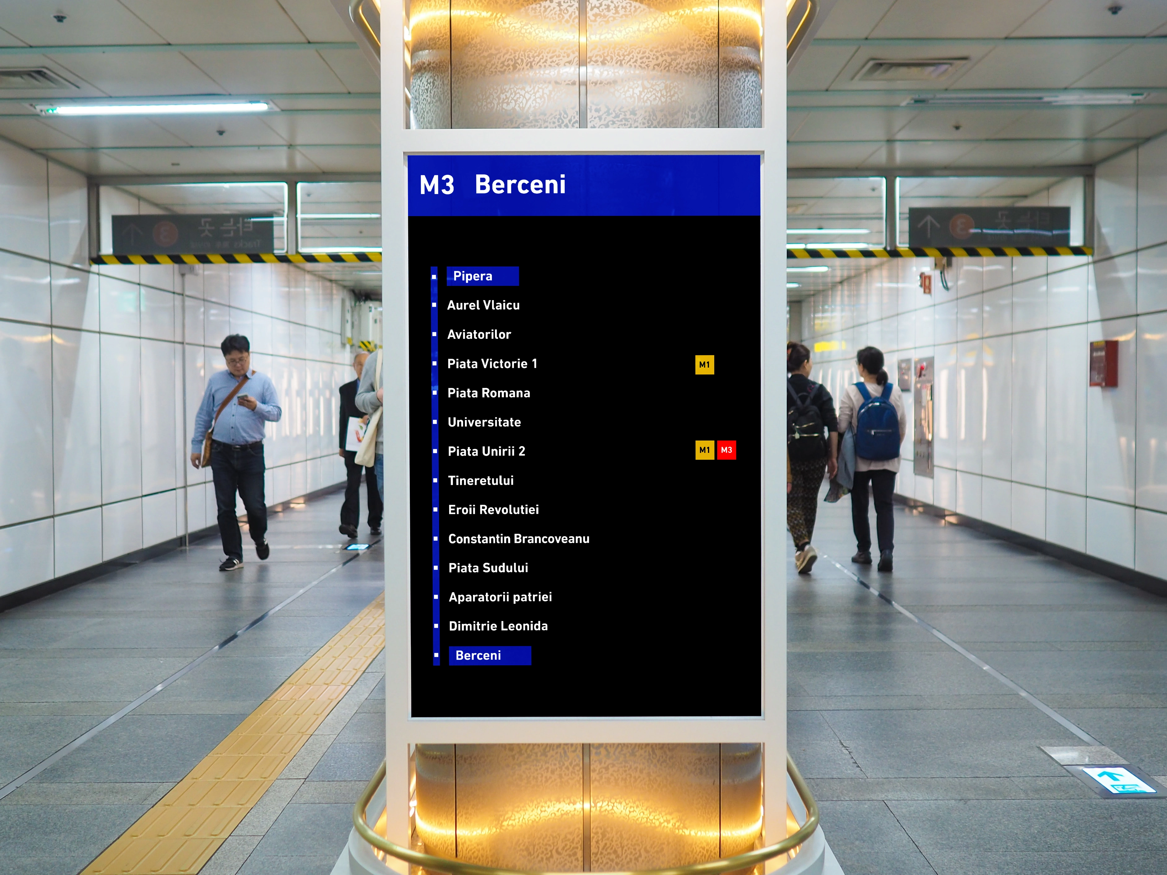 Modern subway station sign with illuminated pillars and people walking.
