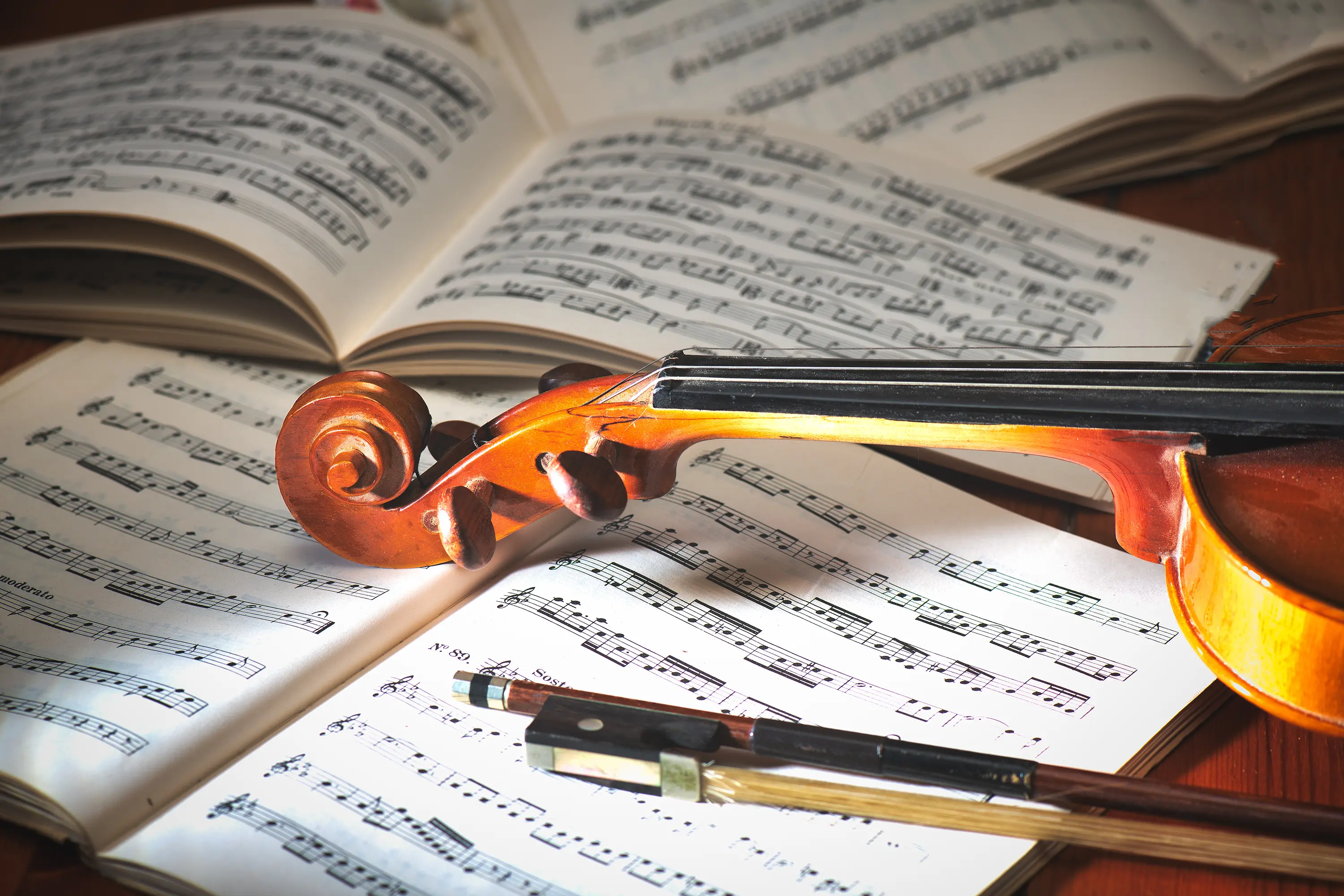 Close-up of a violin scroll and bow on sheet music, warm lighting, artistic photography.