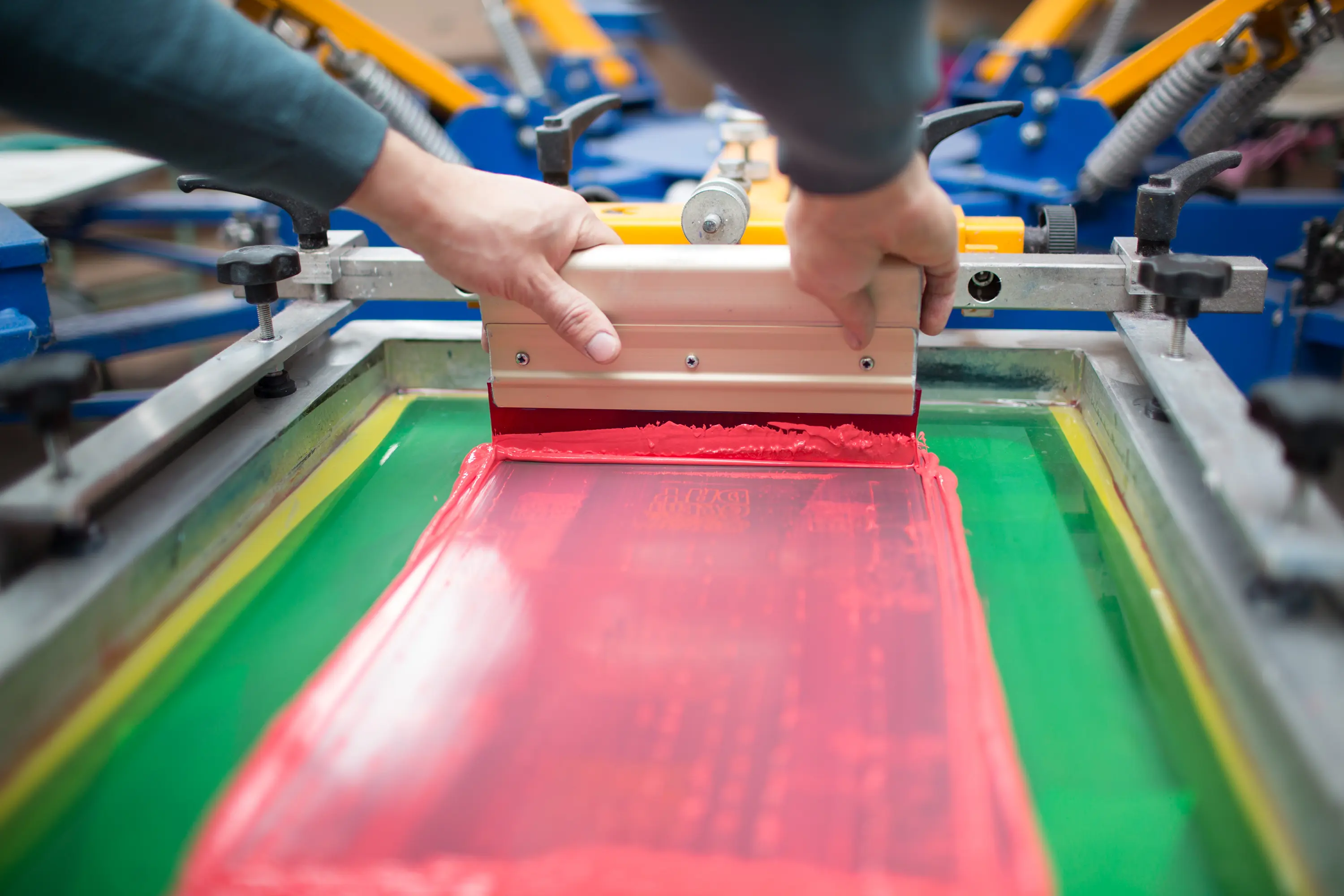 Screen printing process: hands applying red ink with squeegee on silk screen.