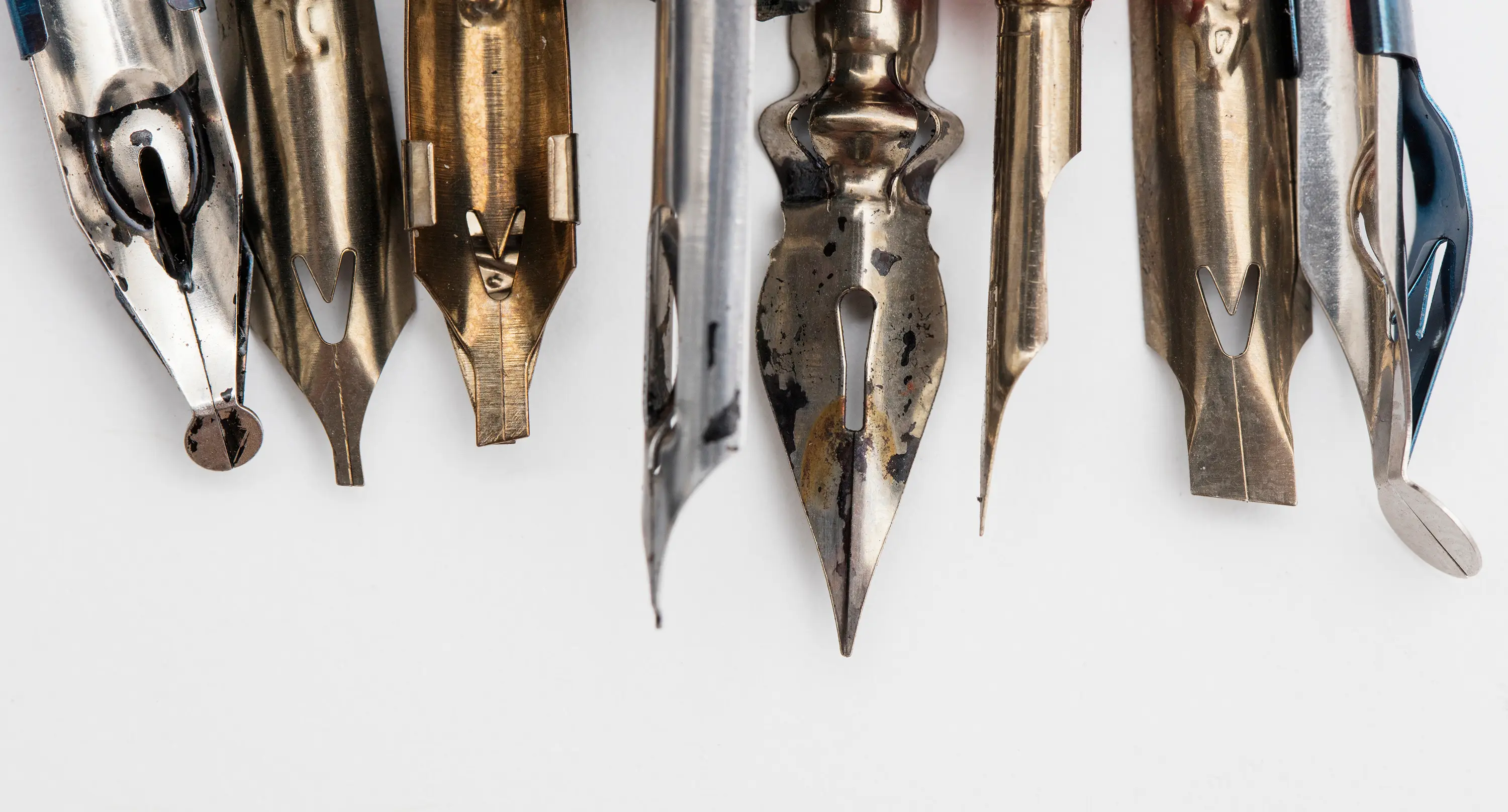 Close-up of vintage metal calligraphy nibs on a white background.