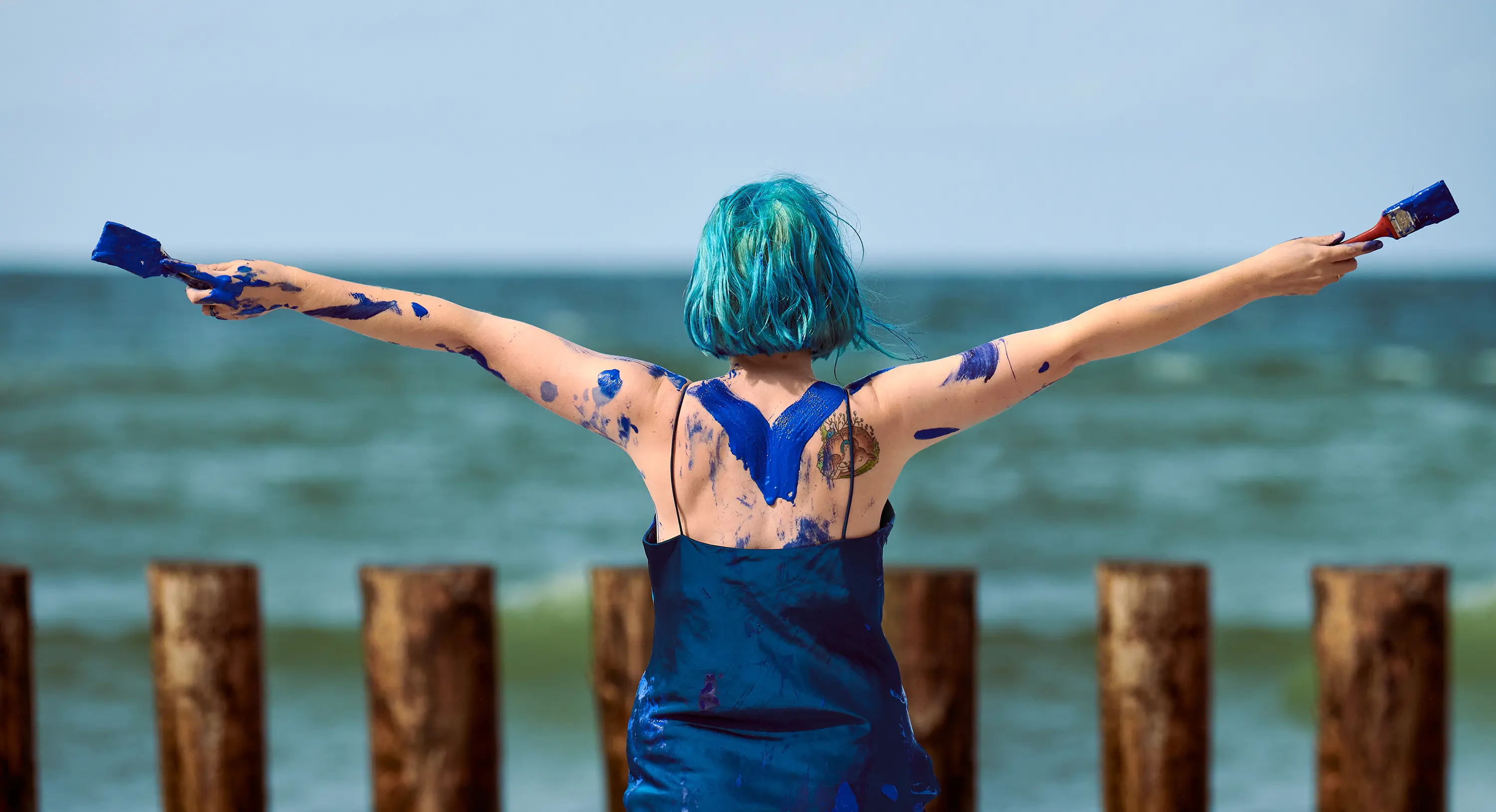 Abstract body painting with blue paint and brushes on a beach.