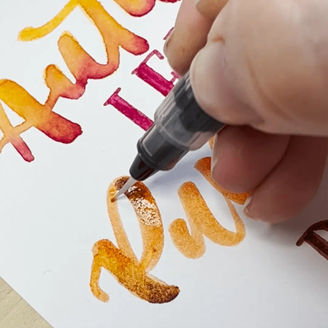 Watercolor calligraphy with brush pen, warm tones, artistic process.