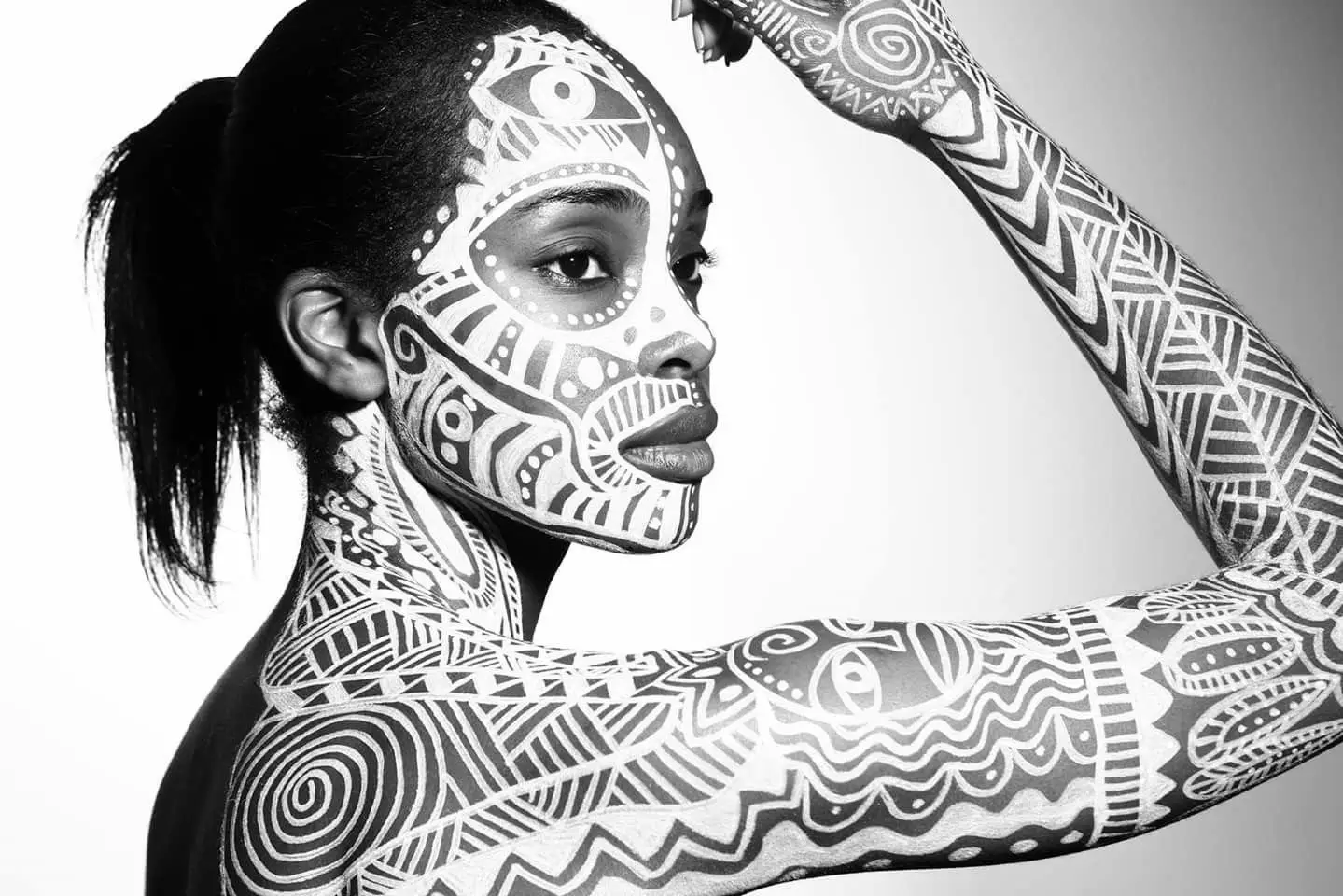 Black and white portrait of a woman with intricate white tribal body paint.