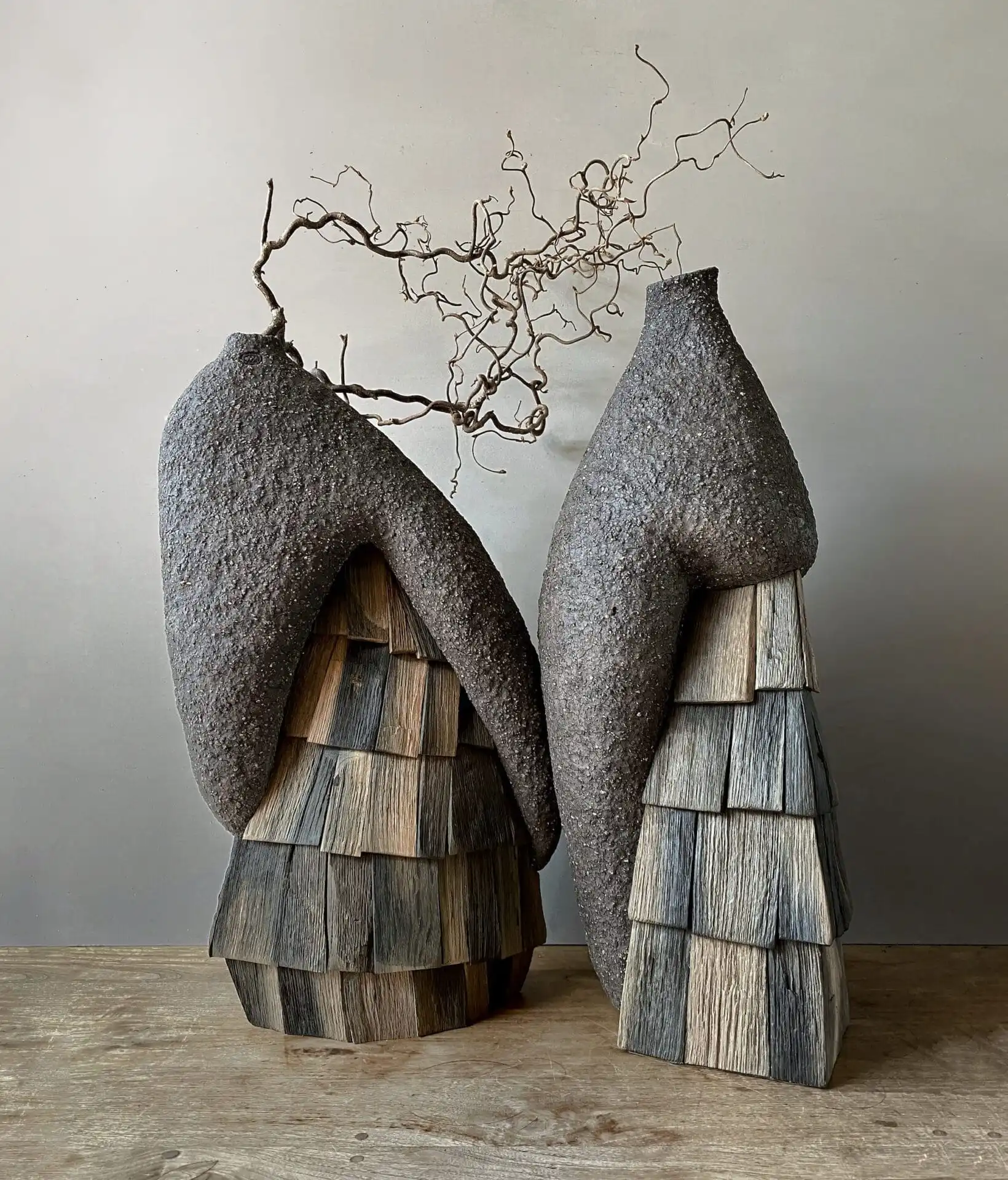 Textured ceramic sculptures with wood accents and branches, evoking organic forms.